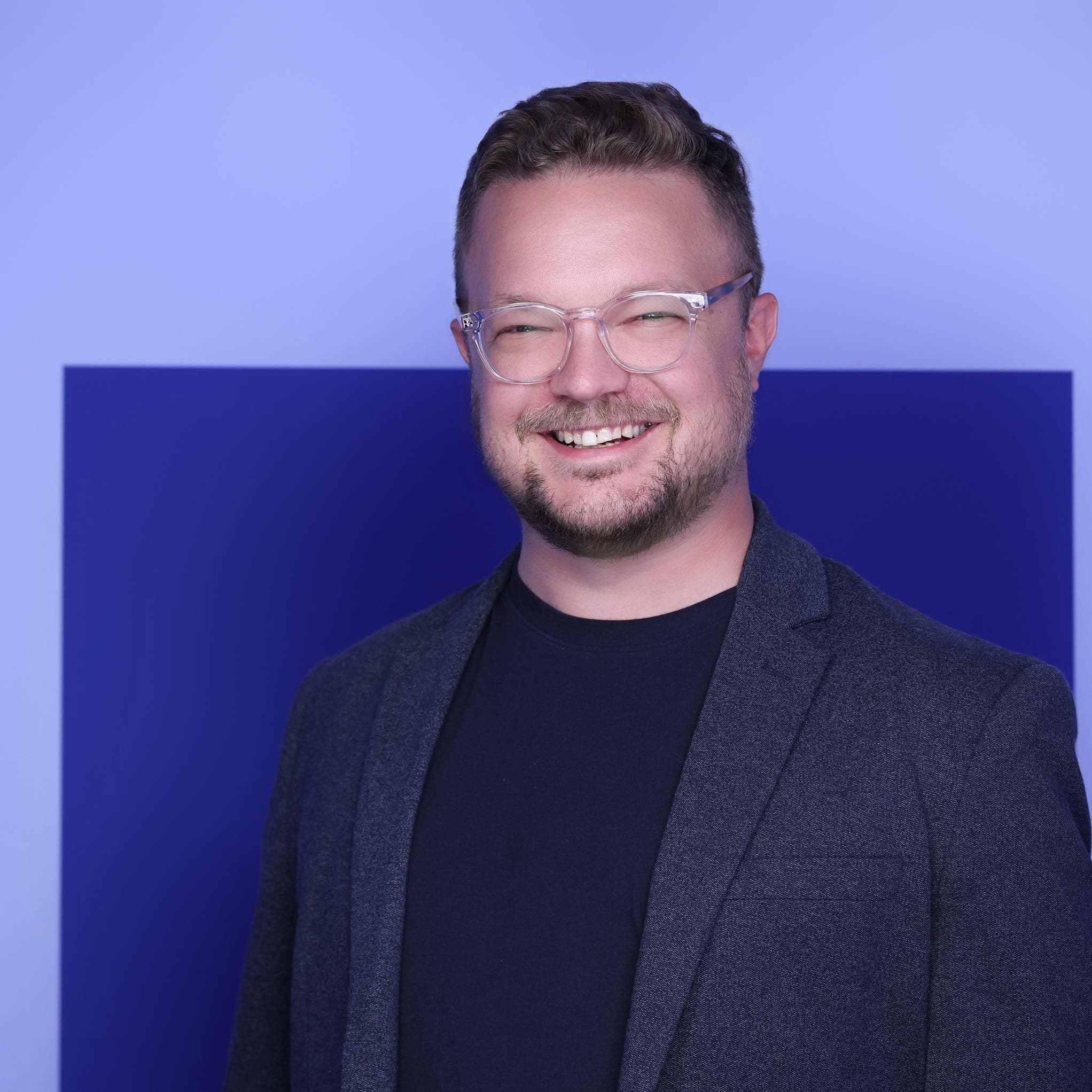 Mike Thibideau smiling, wearing glasses and a dark blazer